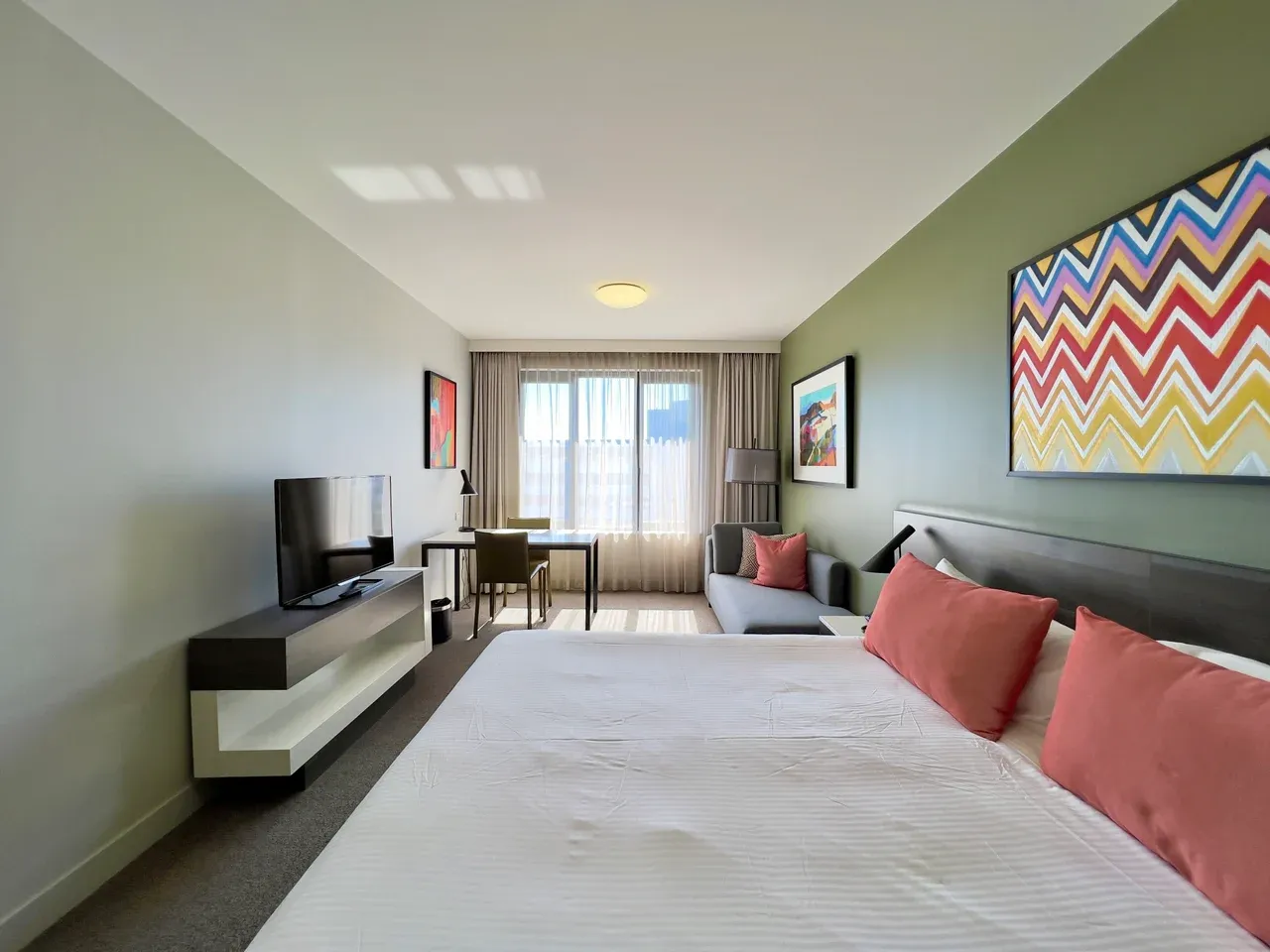 Furnished accommodation room in Sydney, Australia, with a bed, sofa, television and table beside a curtained window