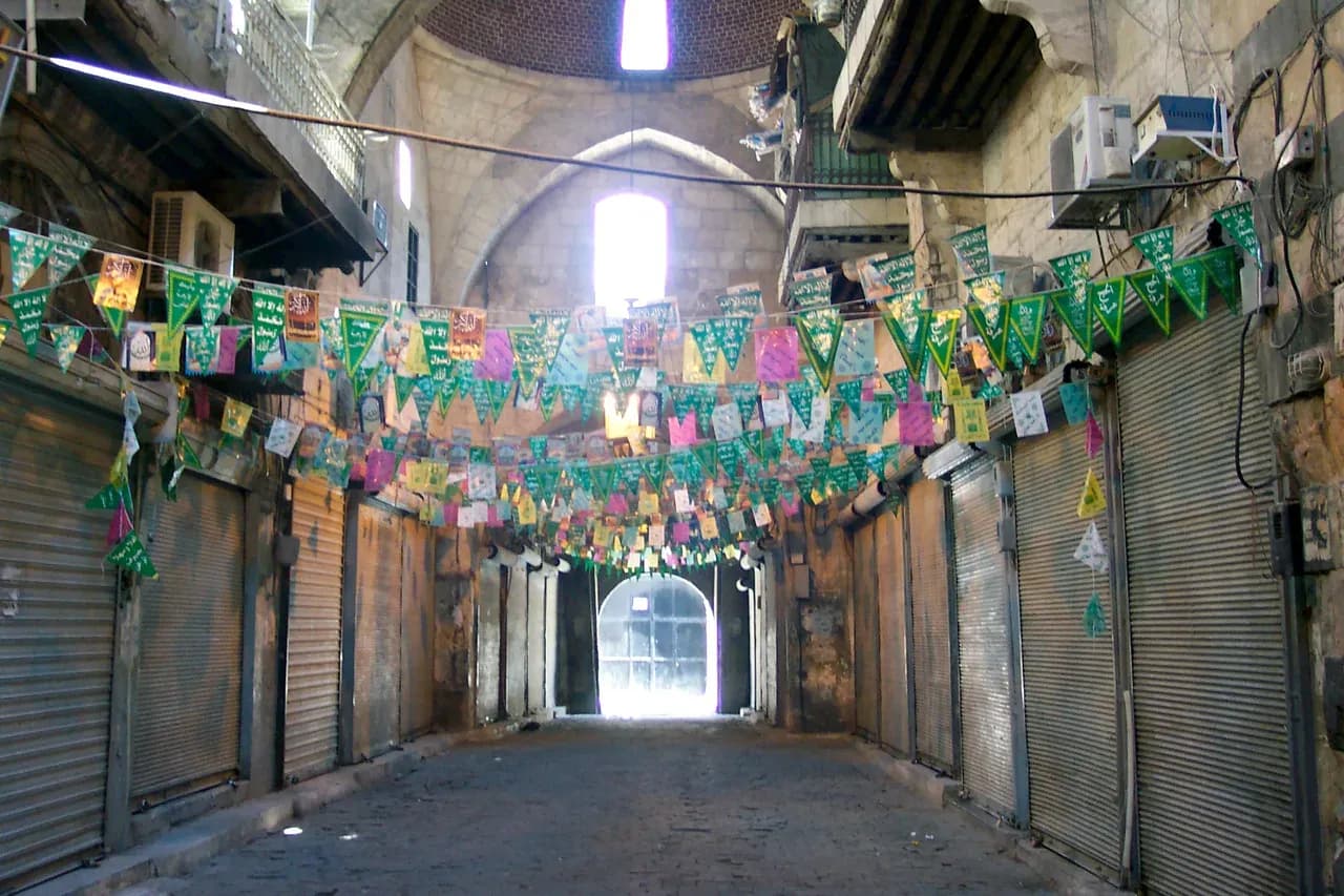 Covered passage in Aleppo’s Suq al-Farrayin with closed shop shutters and coloured decorations, photographed in 2005.