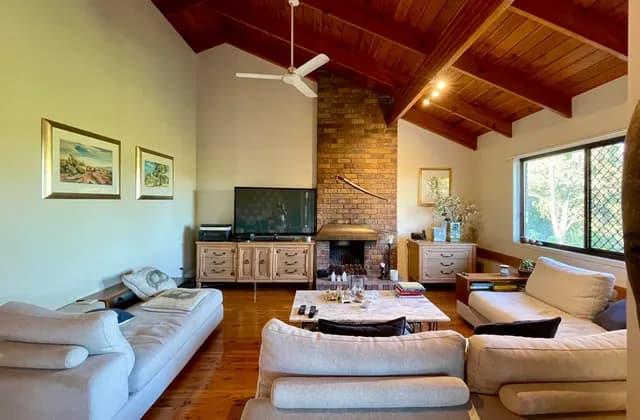 Furnished sitting room in Corinda, Queensland, Australia with sofas, a brick fireplace, exposed ceiling beams and a window