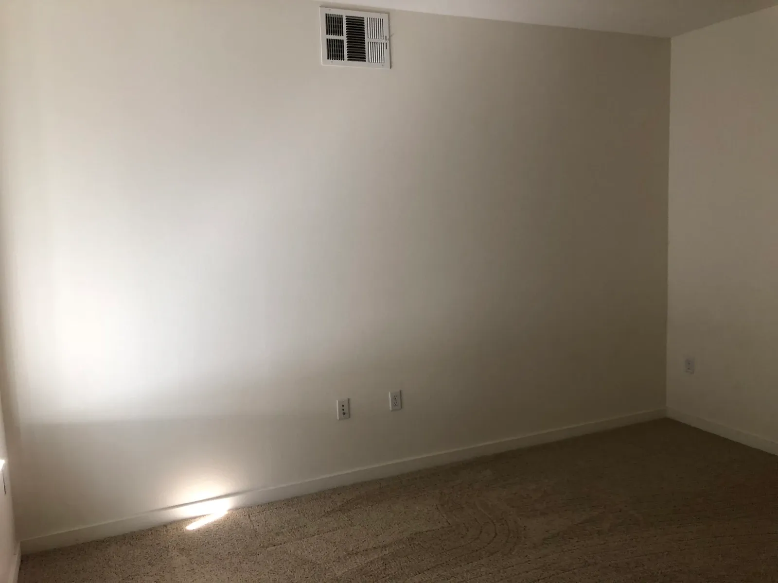 Unfurnished apartment corner with uninterrupted wall space, sockets and carpet, illustrating questions about furniture and storage