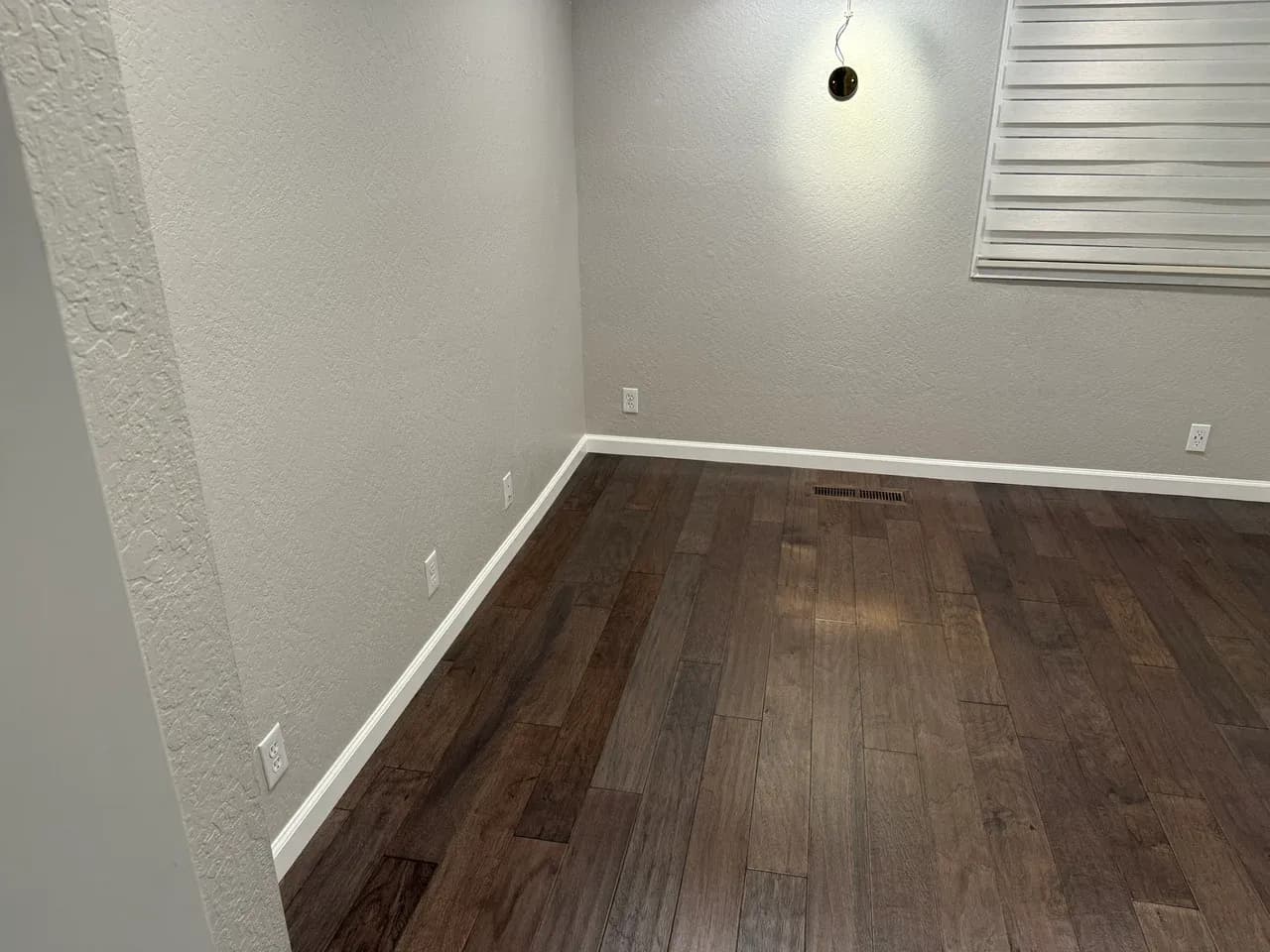 Unfurnished apartment room with a projecting wall, blind-covered window and wood-effect flooring