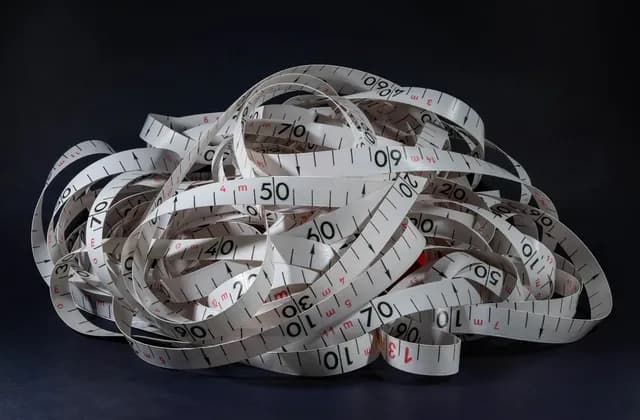 Loops of a white measuring tape with black and red markings against a dark background
