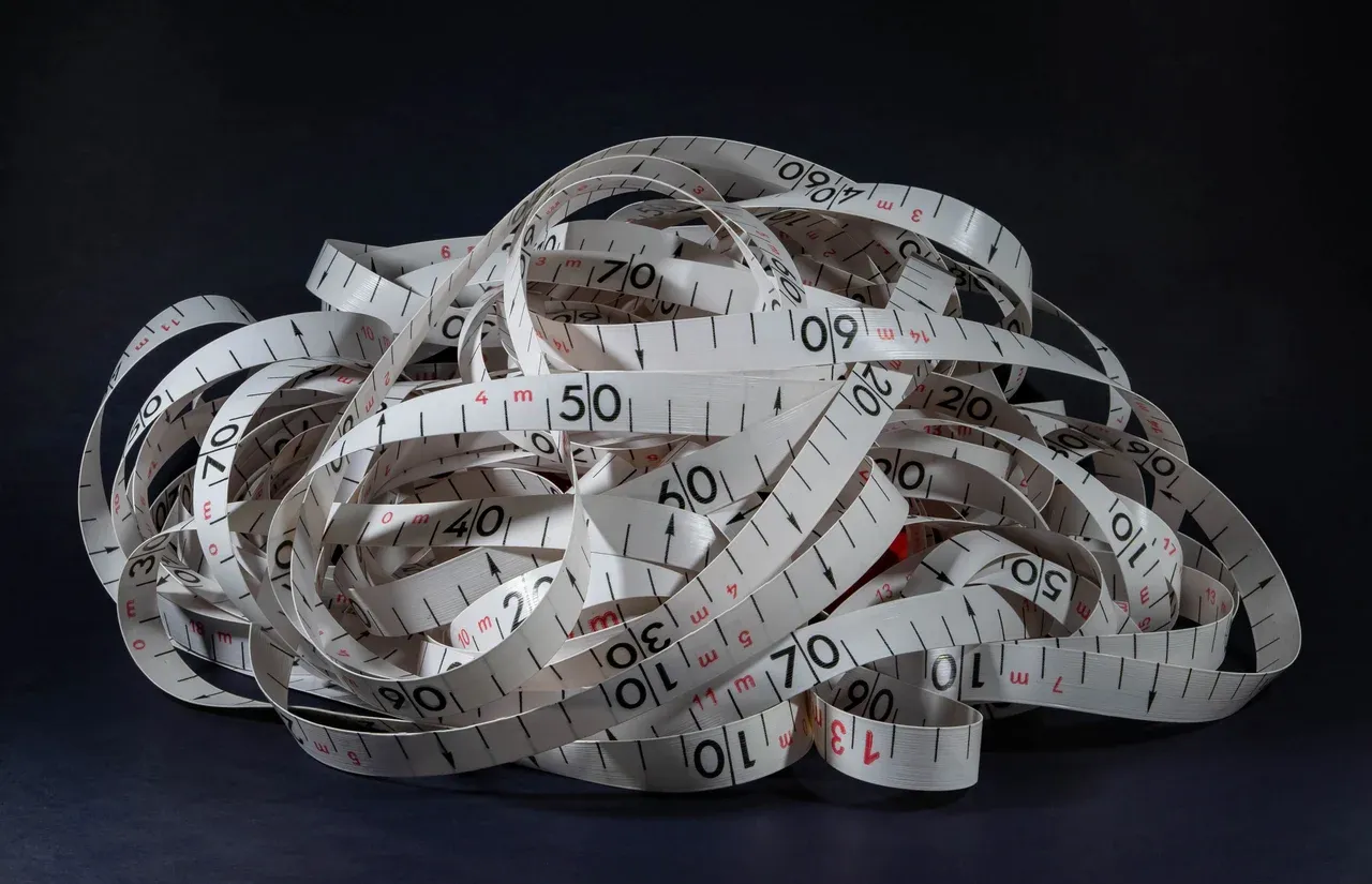 Loops of a white measuring tape with black and red markings against a dark background