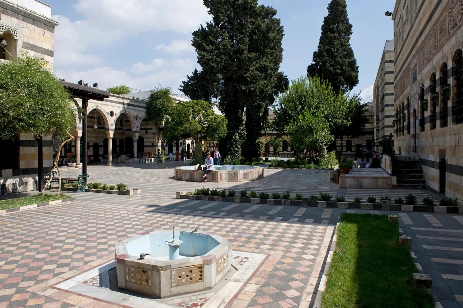 Wide view across patterned paving, basins, trees and surrounding buildings at Azem Palace, Damascus, September 2008