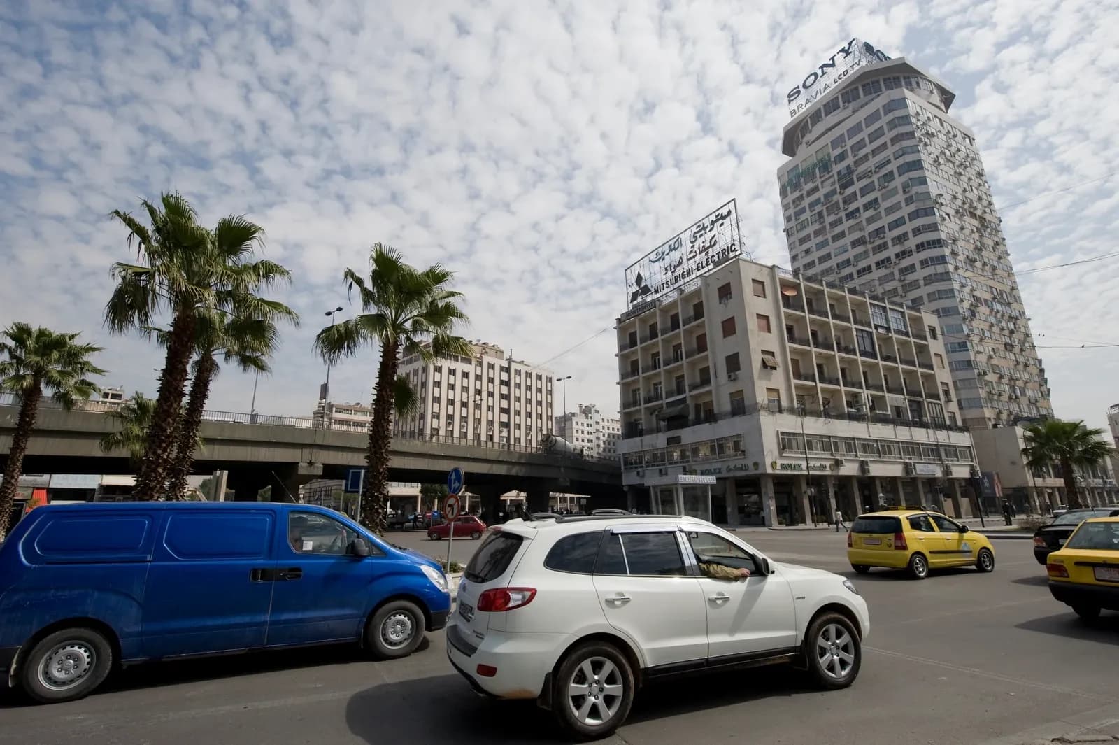 Tall buildings, palm trees and vehicles by Barada street in Damascus, April 2009