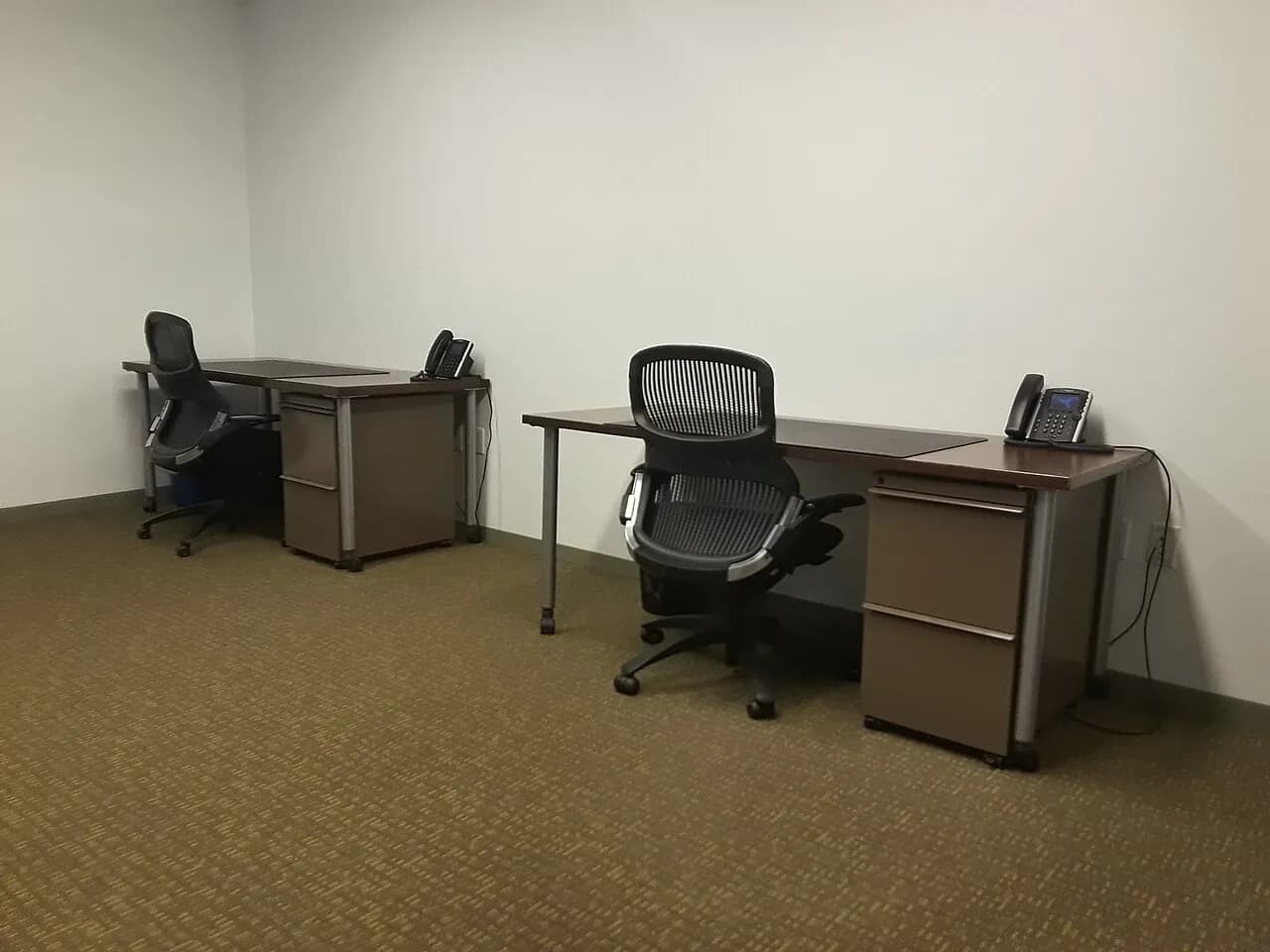 Two desks with office chairs and telephones in an unoccupied coworking office, photographed in December 2021