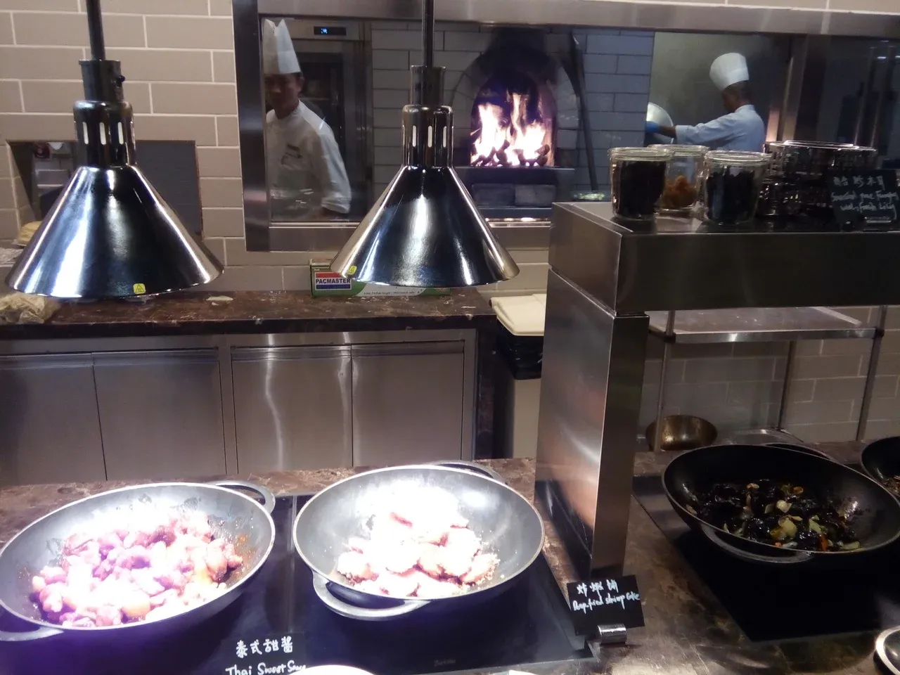 Buffet counter with warming lamps, food pans and staff visible through kitchen windows in Macau