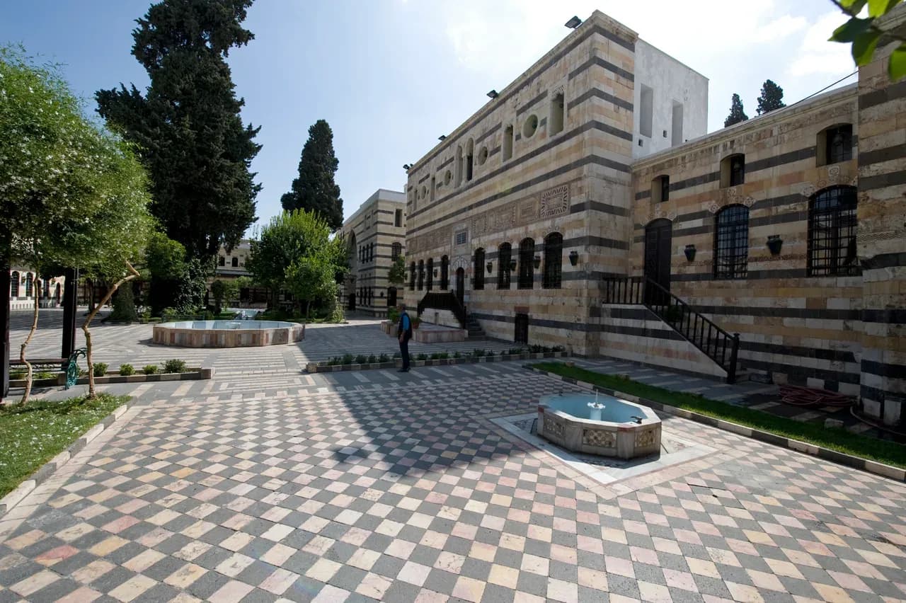 Azem Palace courtyard in Damascus with patterned paving, a fountain and a striped stone facade, photographed in 2008.