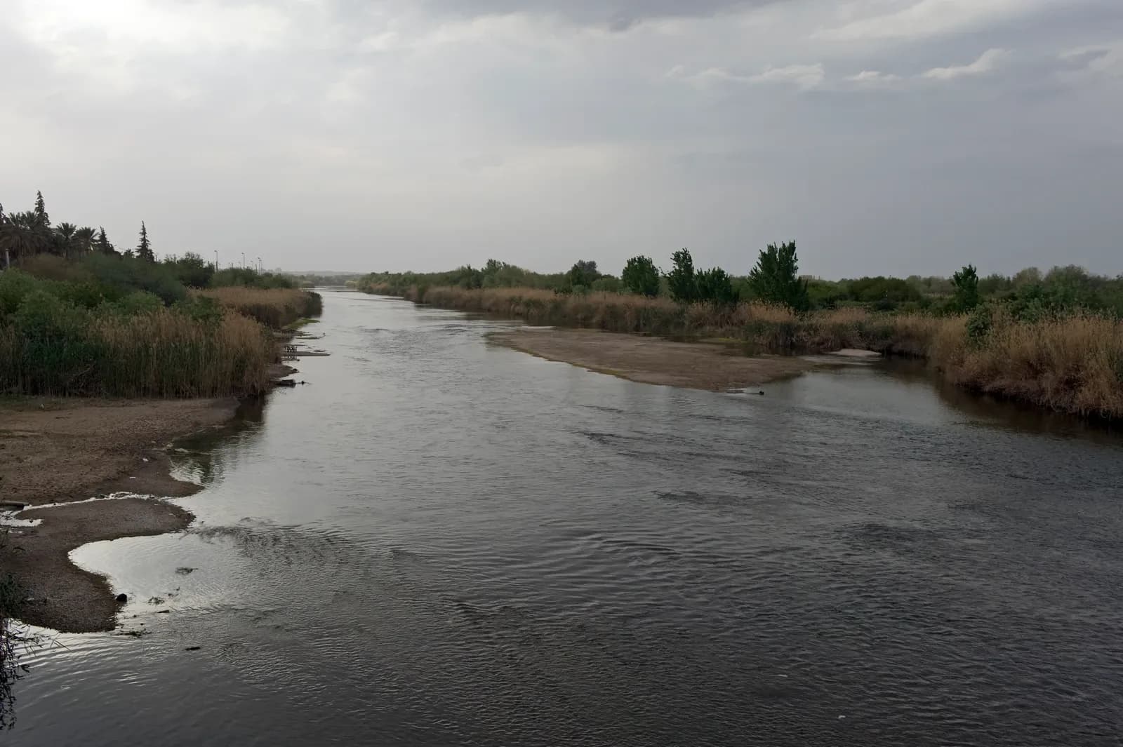 Euphrates water channel bordered by exposed shore, reeds and trees in Deir ez-Zor, April 2009