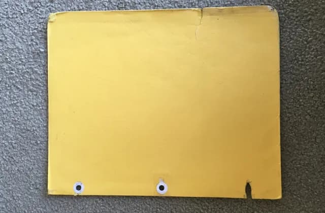 Worn yellow file folder with punched holes on a grey carpet, photographed in December 2014