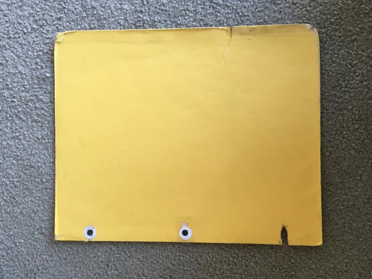 Worn yellow file folder with punched holes on a grey carpet, photographed in December 2014
