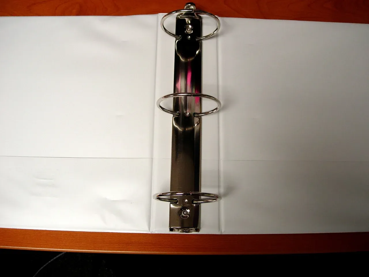 Open empty ring binder with three metal rings on a wooden surface