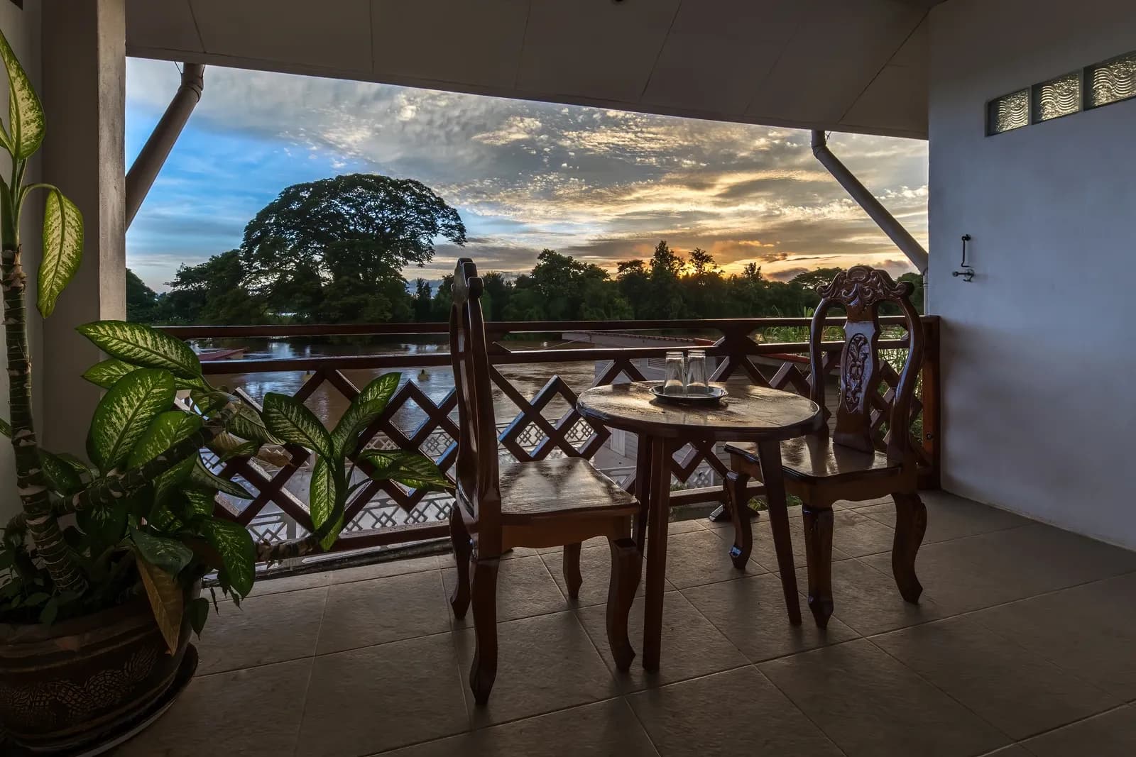 Wooden table and chairs beside a balcony railing overlooking the Mekong at sunrise in Don Det, Laos, July 2022