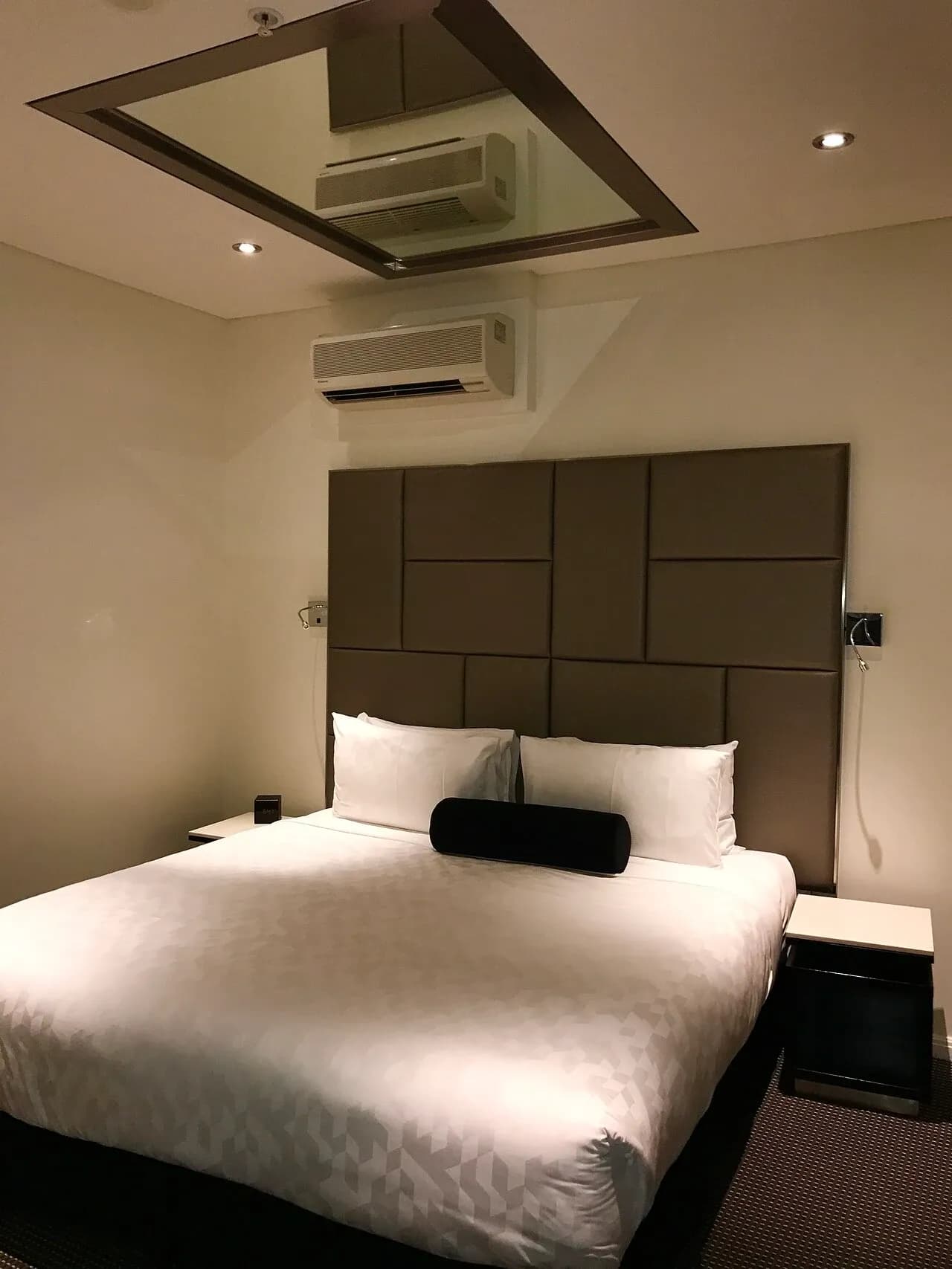 Bed, padded headboard, bedside tables and wall-mounted cooling unit in serviced accommodation in Sydney, Australia