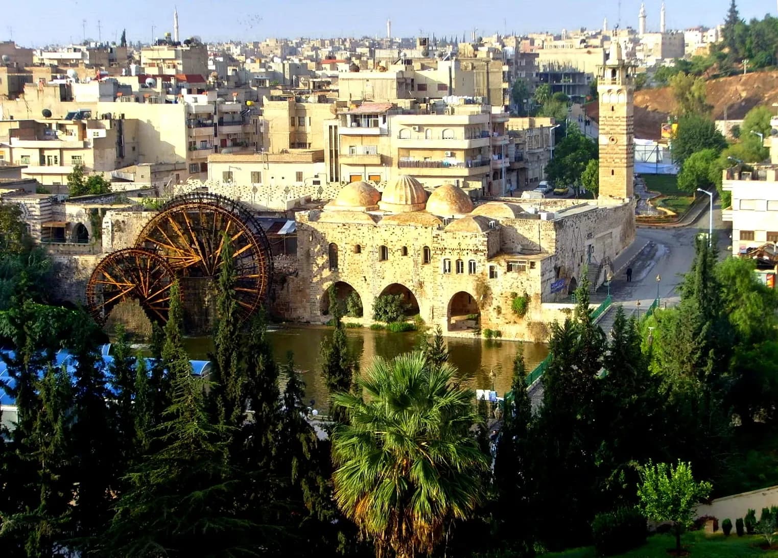 A wooden waterwheel beside historic stone architecture and urban blocks in Hama, October 2008 archive photograph