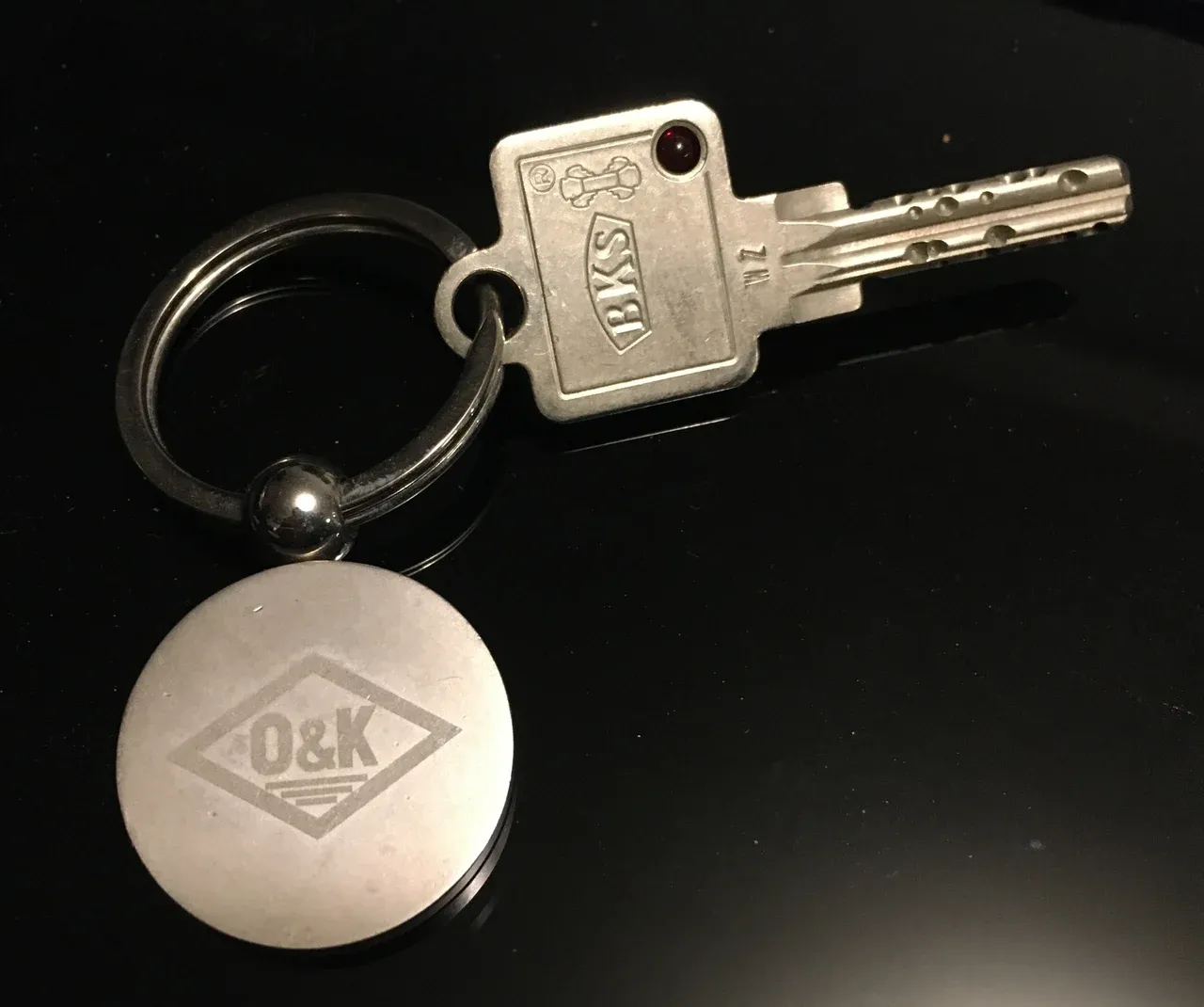 Single metal door key on a circular keyring with a round branded fob against a dark background