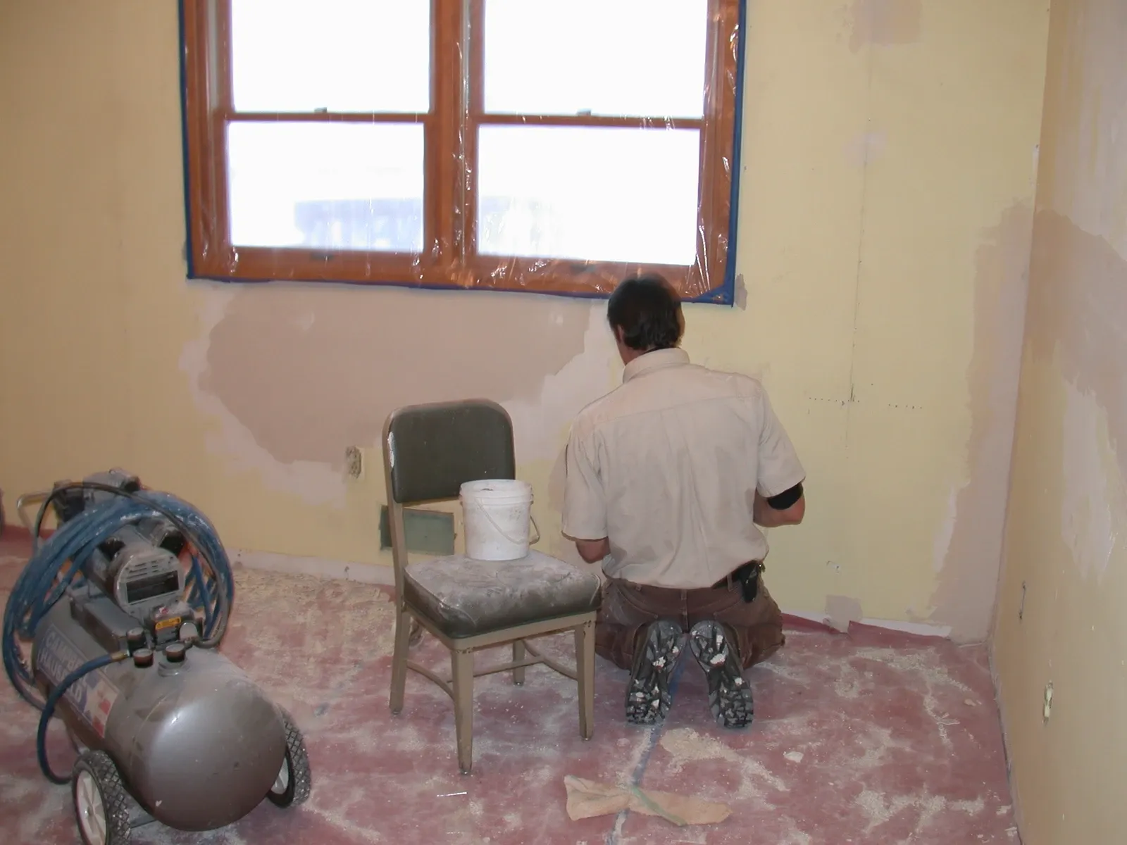 Worker kneeling beside patched interior walls beneath a window at Garrison Dam hatchery quarters, January 2011