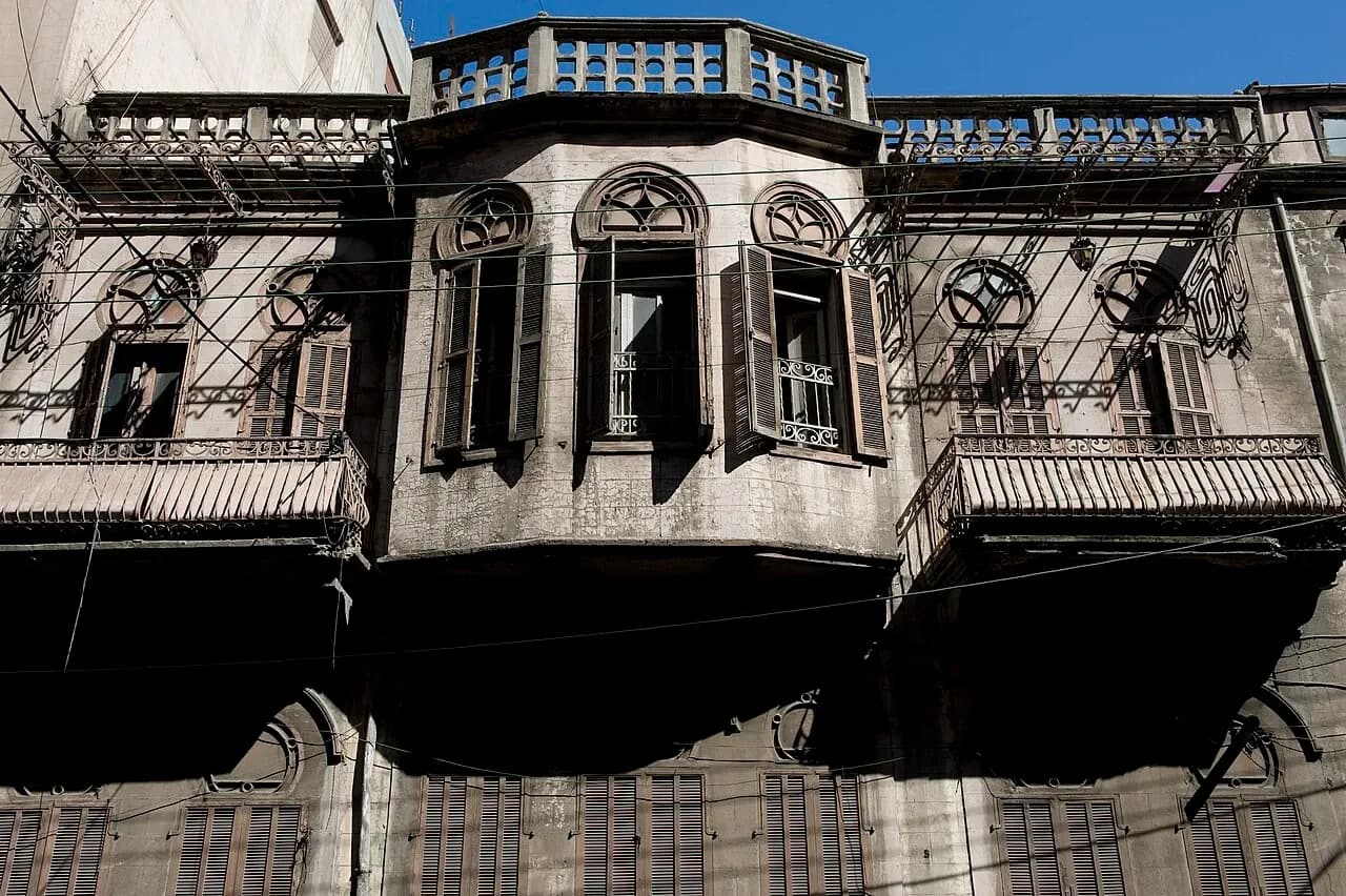 Homs stone facade with shuttered arched windows, wrought-iron balconies and a projecting central bay