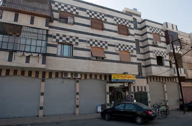 Striped building facade with enclosed window grilles and ground-floor shops in Homs, photographed in October 2010