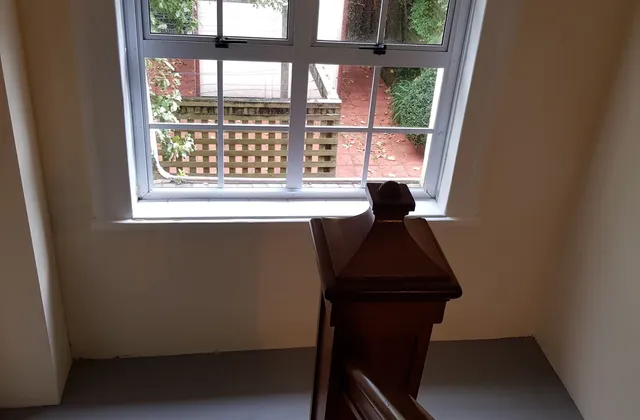 Multi-pane staircase window with a timber handrail and trees visible outside at Chevening Flats