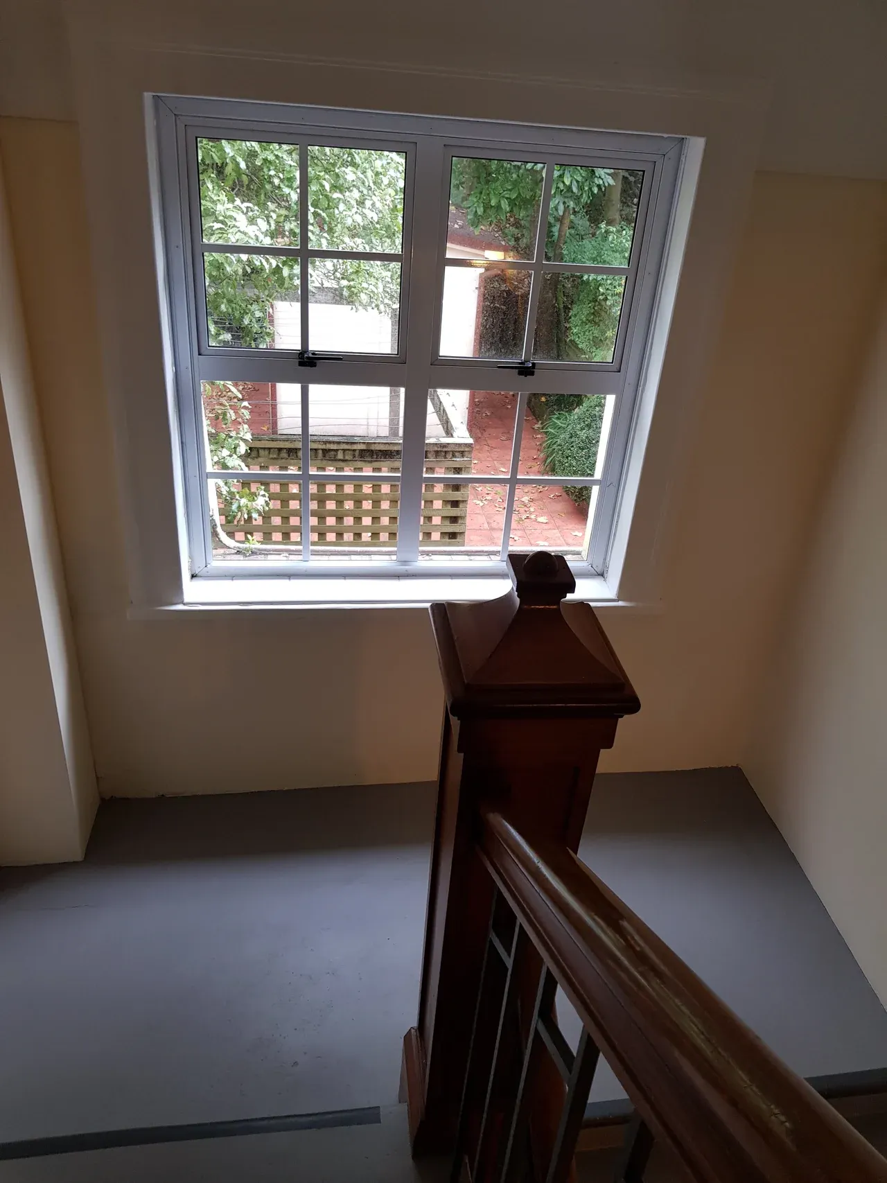 Multi-pane staircase window with a timber handrail and trees visible outside at Chevening Flats