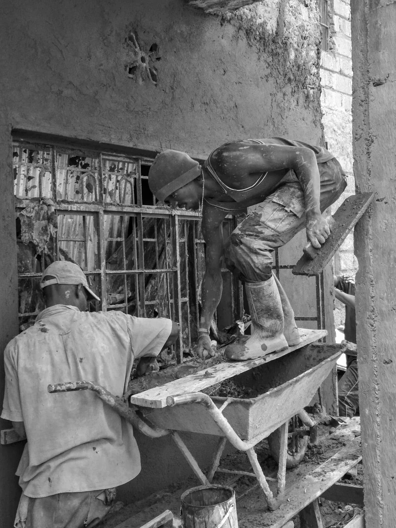 Workers beside an unfinished wall and window opening at a residential construction site in Kenya