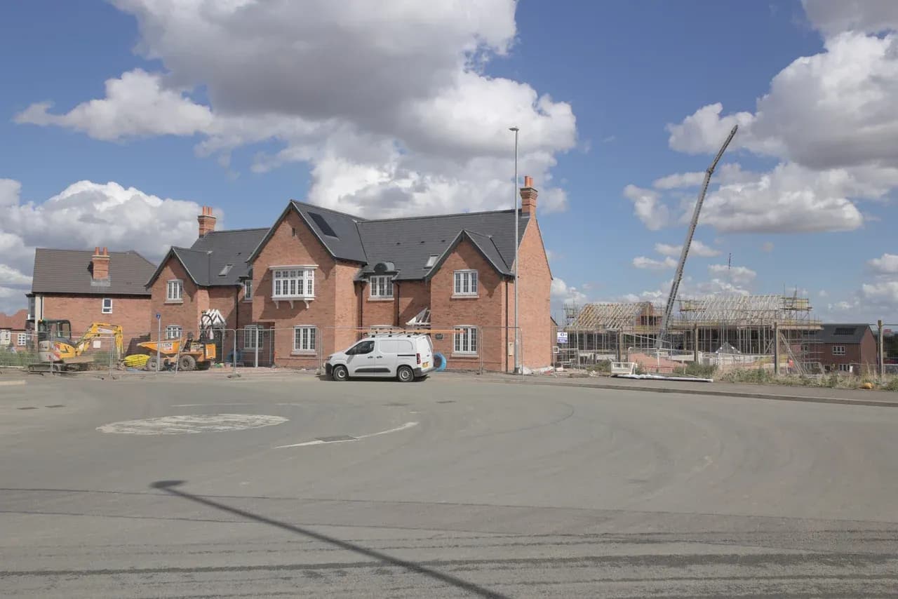 Brick houses and adjoining houses under construction in Broadnook, with scaffolding, exposed roof framing, vehicles and a crane