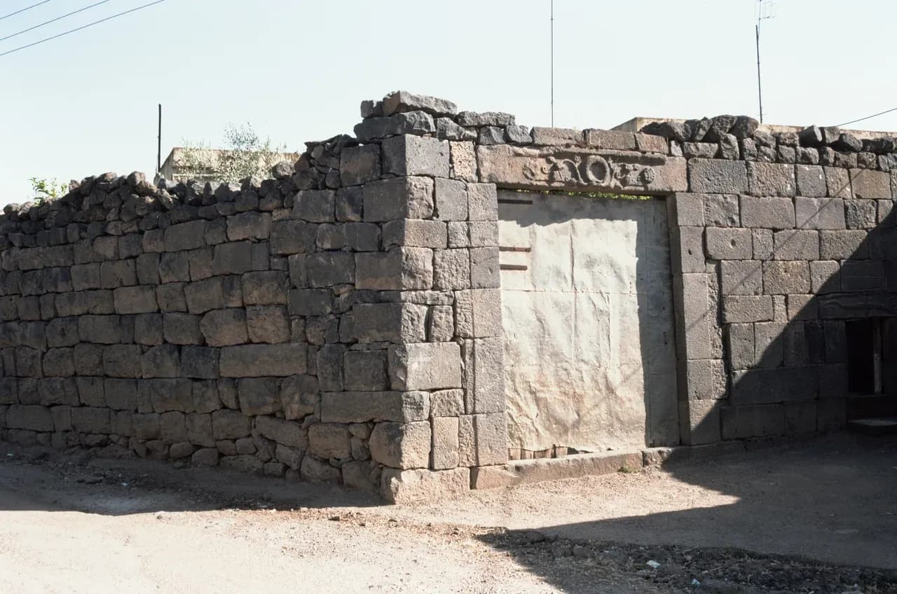 Archive view of a stone wall and buildings in Izra, Daraa Governorate, photographed by Frank Kidner in 1996.