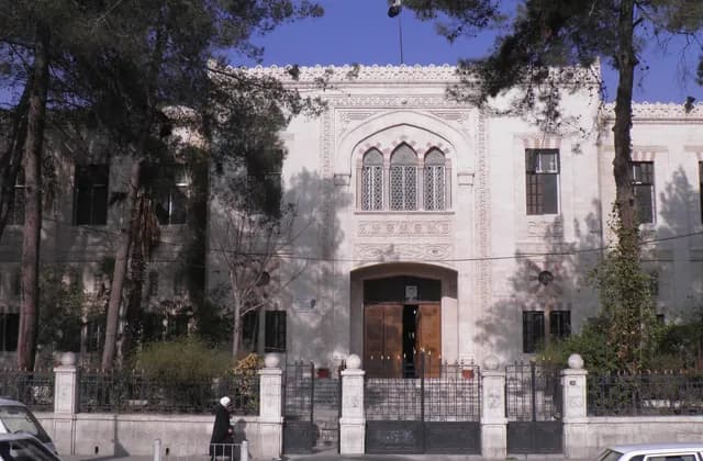 Street facade of Jawdat al-Hashimi School in Damascus, behind trees and vehicles, January 2012