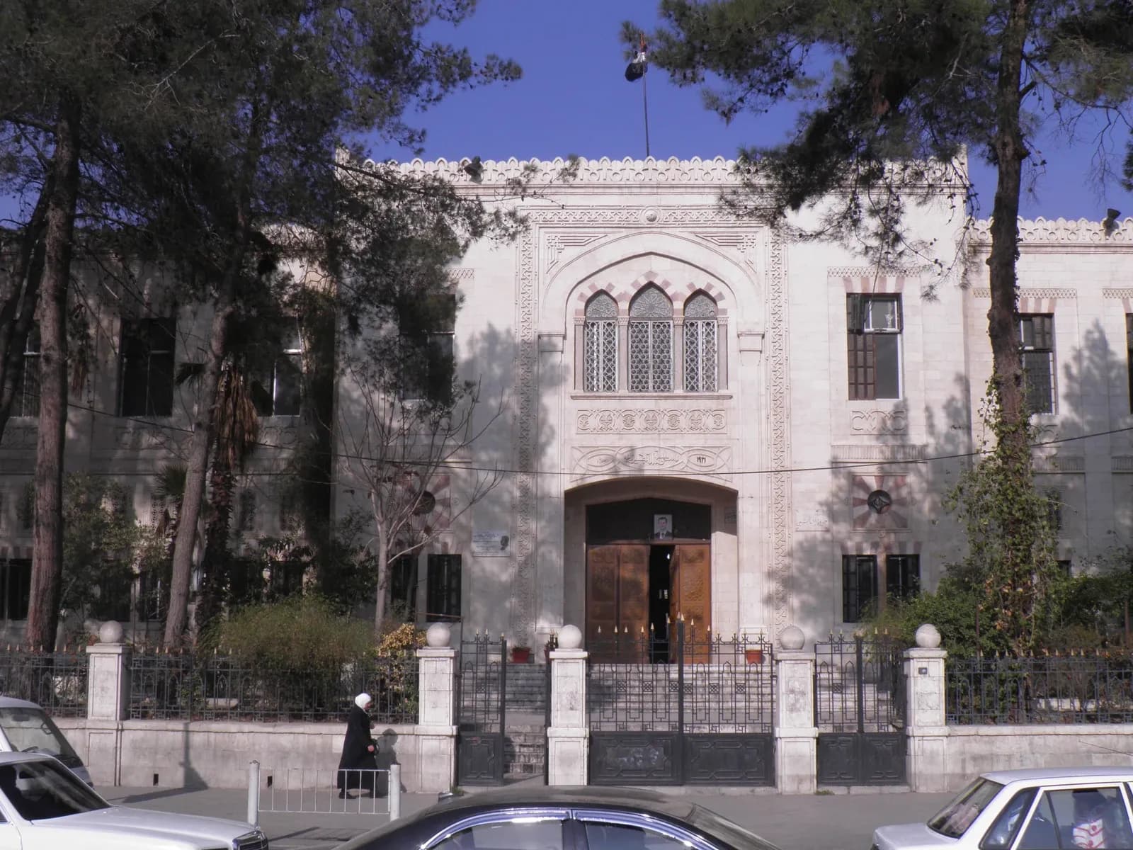 Street facade of Jawdat al-Hashimi School in Damascus, behind trees and vehicles, January 2012