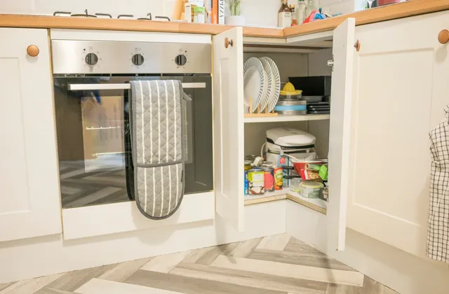 Open white corner kitchen cupboard holding crockery and groceries, photographed in August 2023