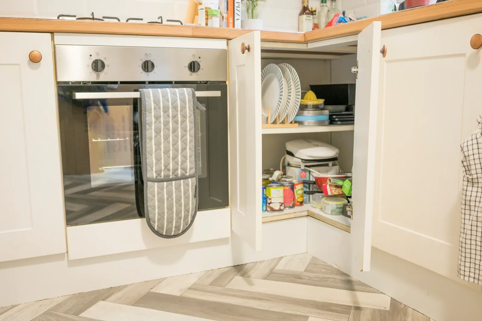 Open white corner kitchen cupboard holding crockery and groceries, photographed in August 2023