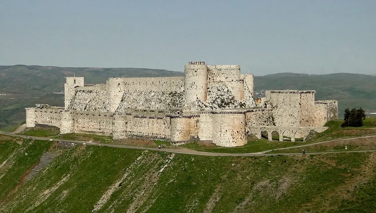 Crac des Chevaliers stone towers and outer fortifications above a green hillside, photographed in April 2010