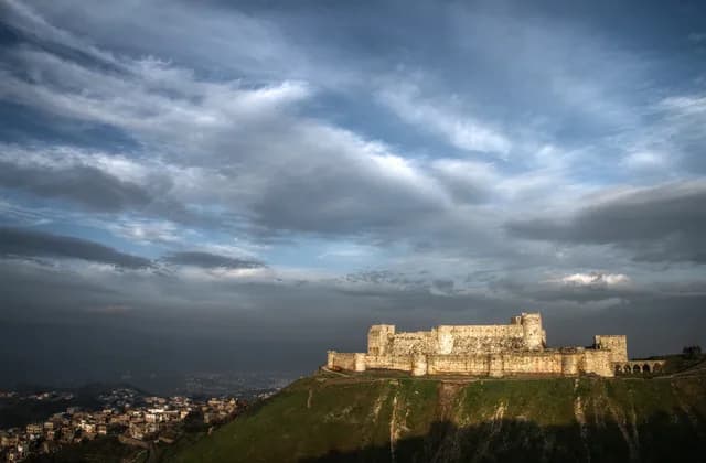 Distant view of Crac des Chevaliers on a hillside above adjoining buildings, January 2010