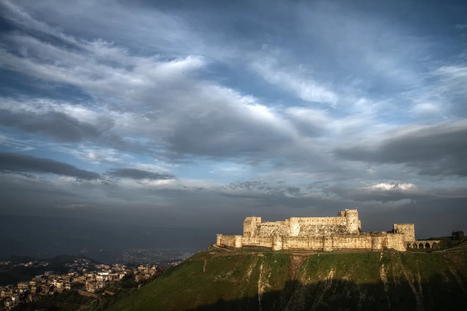 Distant view of Crac des Chevaliers on a hillside above adjoining buildings, January 2010
