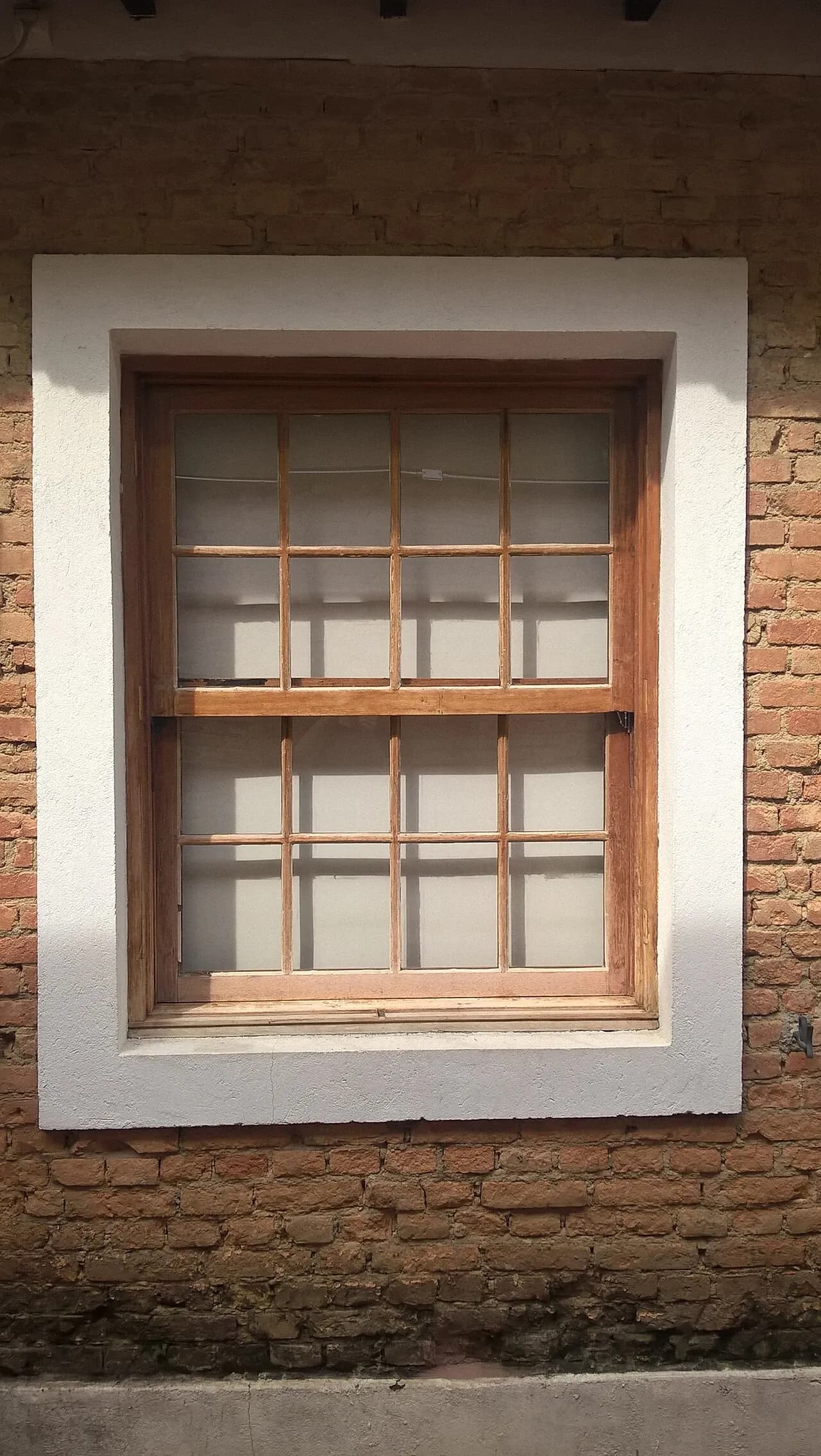 Wooden window with divided panes and light-coloured curtains