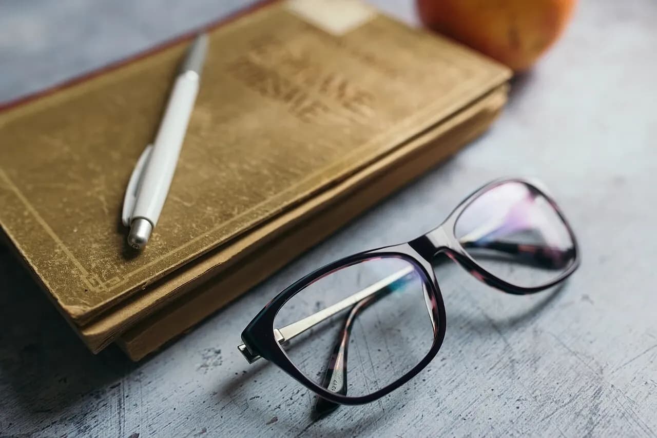Reading glasses and a pen resting on notebooks on a wooden surface