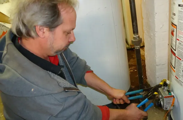 Worker using two hand tools at a fitting beside a water heater