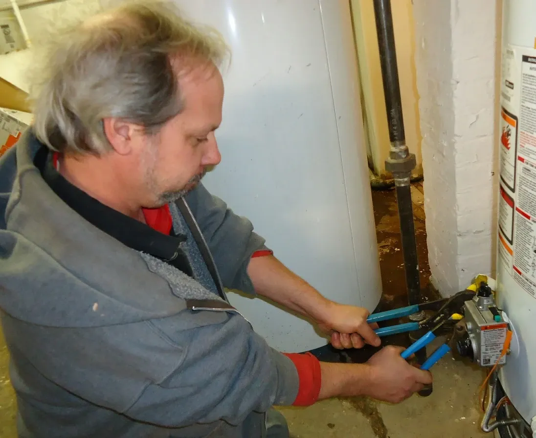 Worker using two hand tools at a fitting beside a water heater