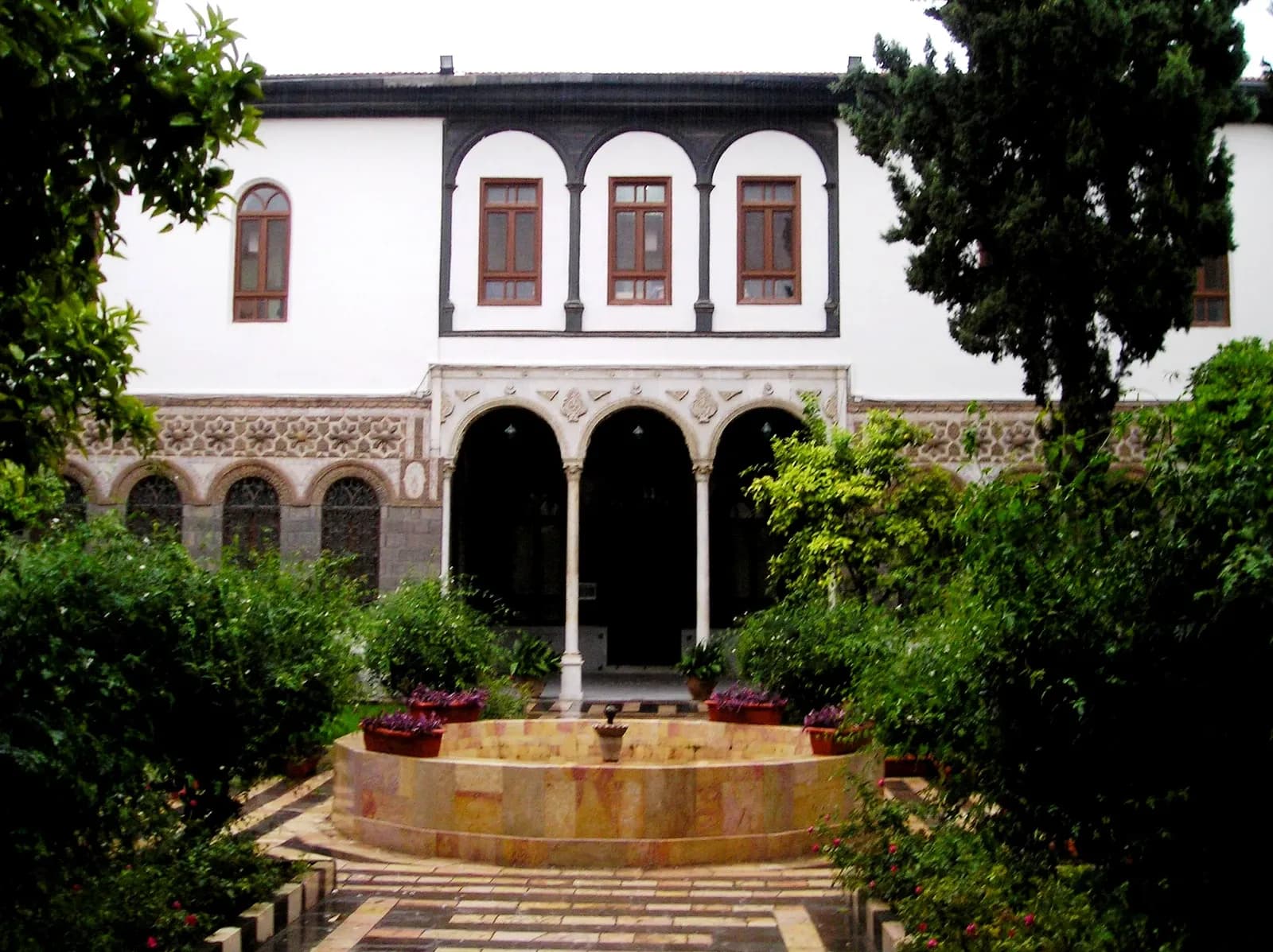 Courtyard of Maktab Anbar in Damascus, with a fountain, planting and arched openings, archive 2009