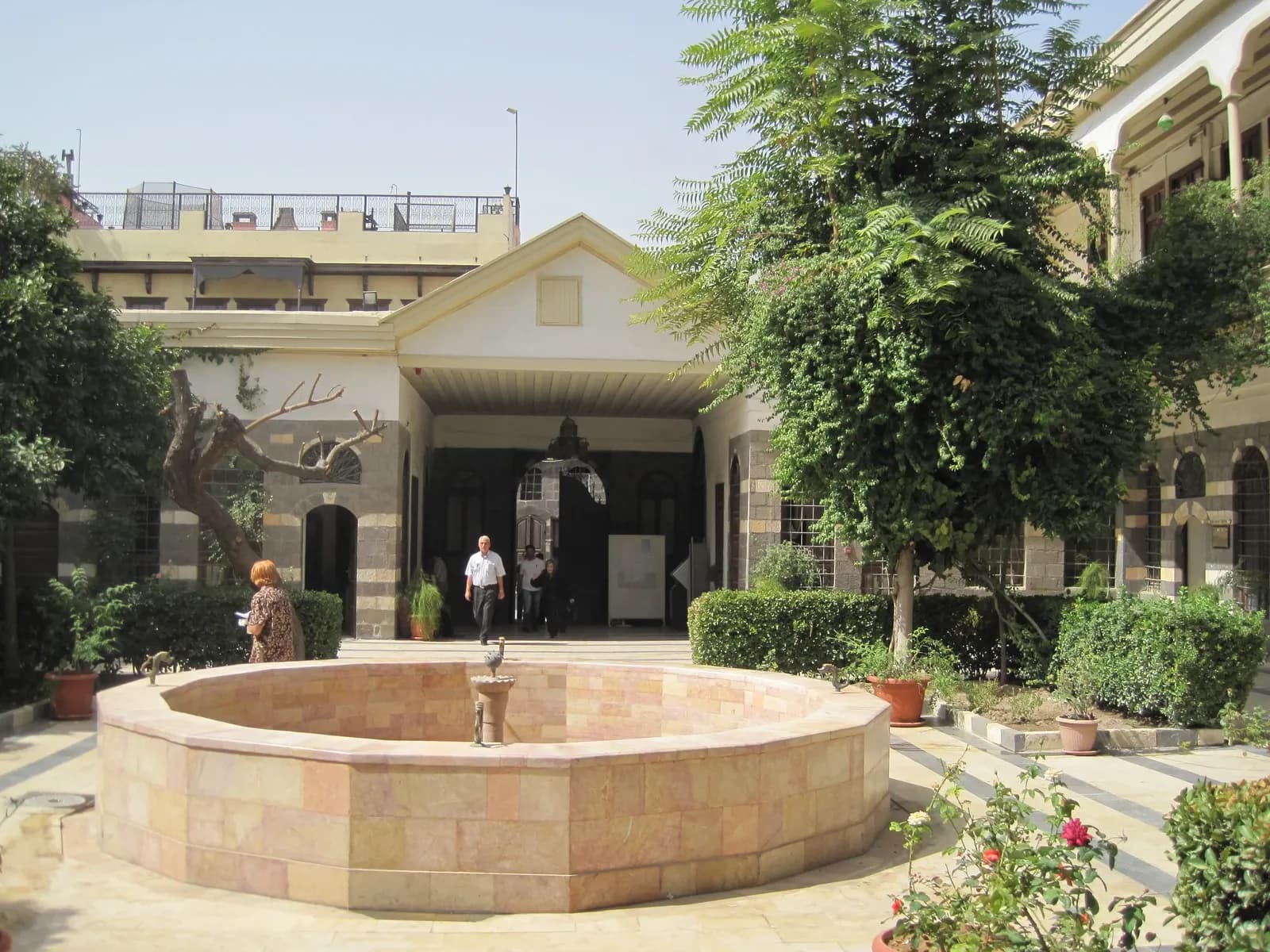Reception courtyard at Maktab Anbar in Damascus, with a circular basin, trees and surrounding facades, October 2010