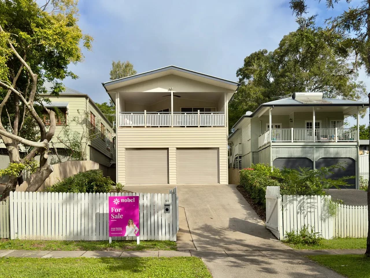 House exterior with a covered balcony, two garage doors and a for-sale sign in Sherwood, Queensland, Australia