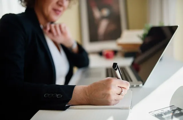 Person writing in a notebook beside an open laptop at a desk, photographed in January 2022