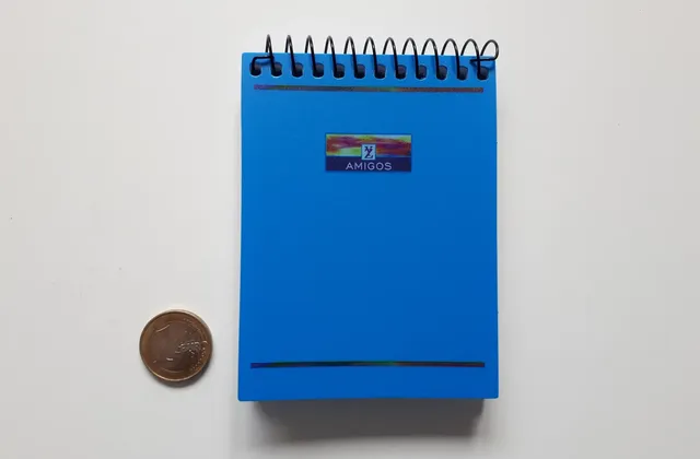 Blue spiral-bound notepad with a coin beside it on a pale surface