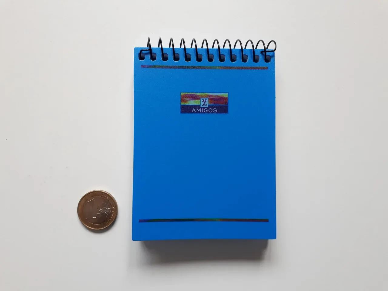 Blue spiral-bound notepad with a coin beside it on a pale surface