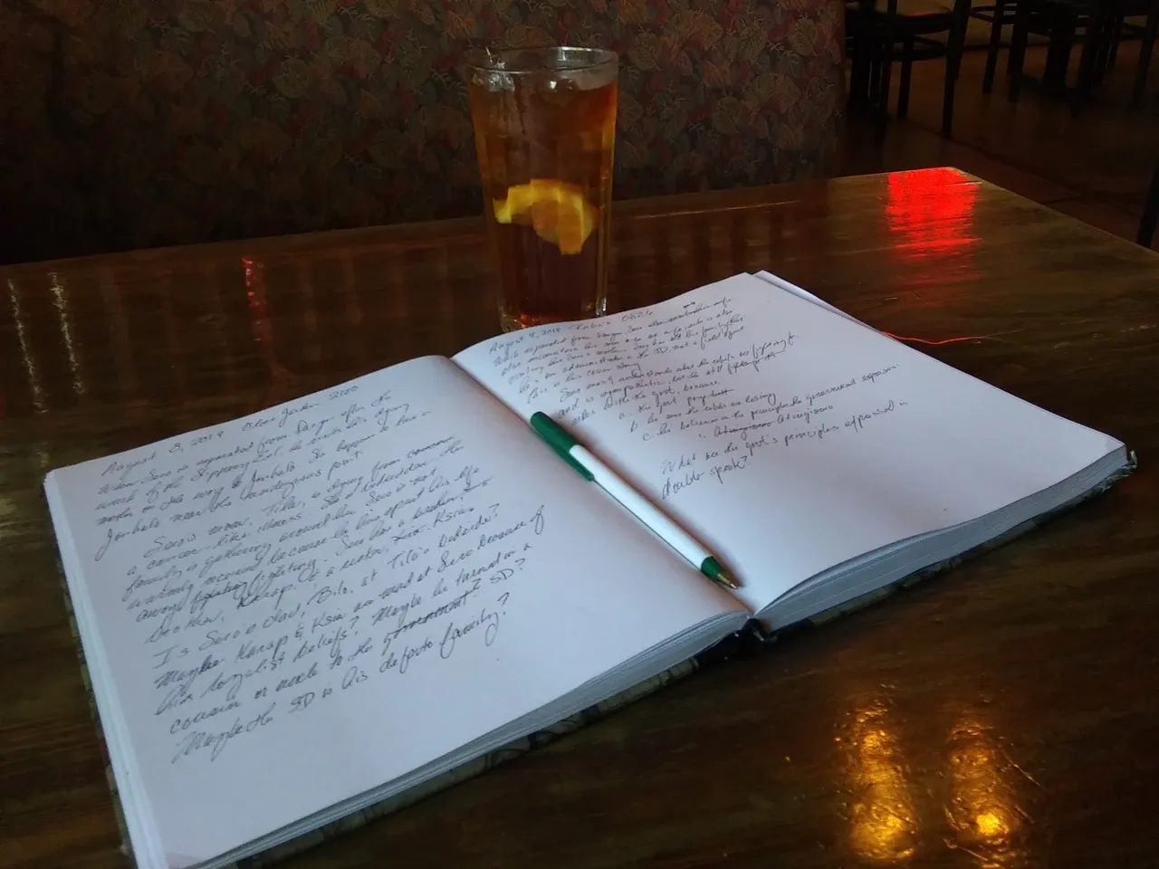 Handwritten pages and a green-and-white pen in an open notebook on a wooden table, photographed in August 2019
