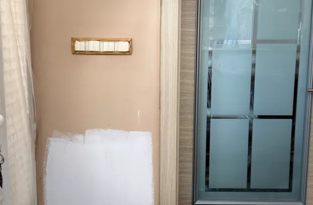 Partly painted interior wall beside a door, with a paint container and tools, May 2026