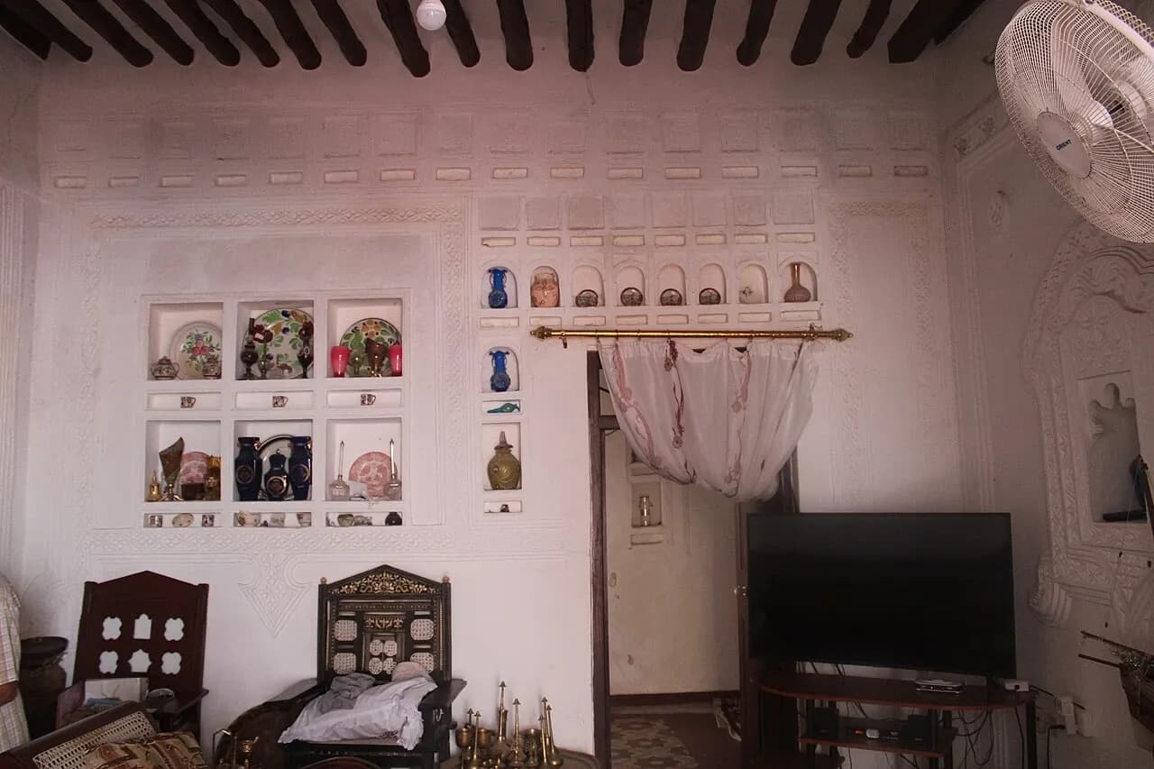 Living-room wall in Kenya with display niches, a curtained doorway, television and ceiling beams, photographed in March 2022