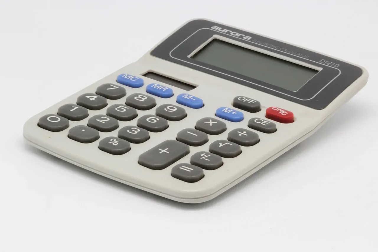 Desktop calculator with grey and blue keys, a red on key and a blank display on a white background