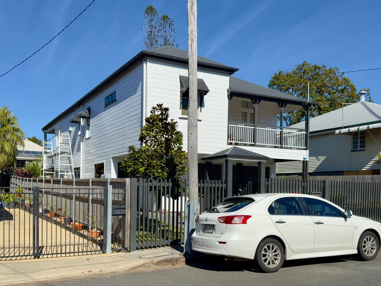 Timber-clad houses behind a fence, with a ladder, utility pole and parked car in Kangaroo Point, Queensland, Australia